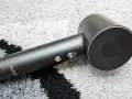 Elegancka, czarna suszarka do włosów Laifen Swift z metalowymi przyciskami, leżąca na szarym dywanie.
