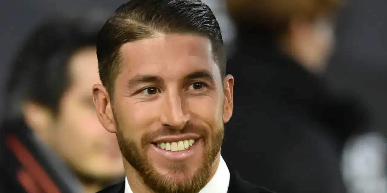 Sergio Ramos z charakterystycznym przedziałkiem z boku, uśmiecha się szeroko, prezentując zarost.