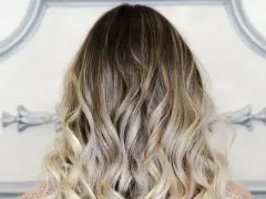 Kobieta z falowanymi włosami w technice sombre, od ciemnego brązu po jasny blond.