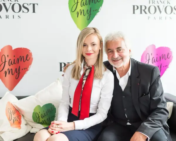 Franck Provost i uśmiechnięta kobieta siedzą na kanapie. W tle logo Franck Provost i serca z napisem "J'aime my...".