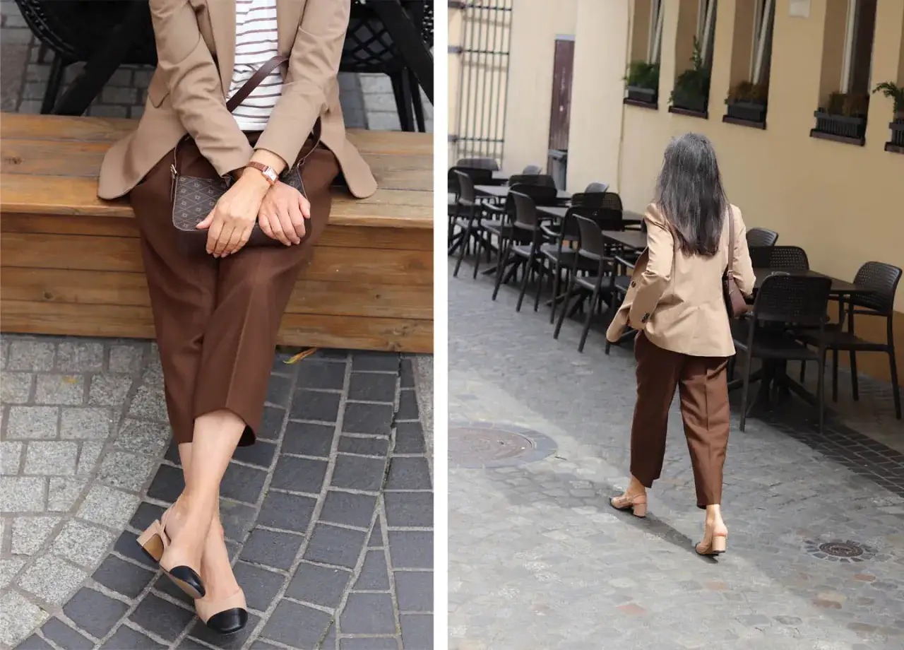 Elegancka kobieta w spodniach w kolorze dark brown jaki to kolor, siedzi na ławce i spaceruje po urokliwej uliczce.
