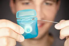 Mężczyzna trzyma niebieskie pudełko z nicią dentystyczną (floss).