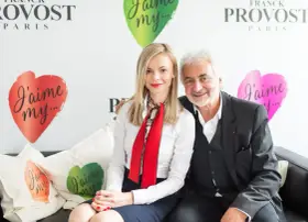 Franck Provost i uśmiechnięta kobieta siedzą na kanapie. W tle logo Franck Provost i serca z napisem "J'aime my...".