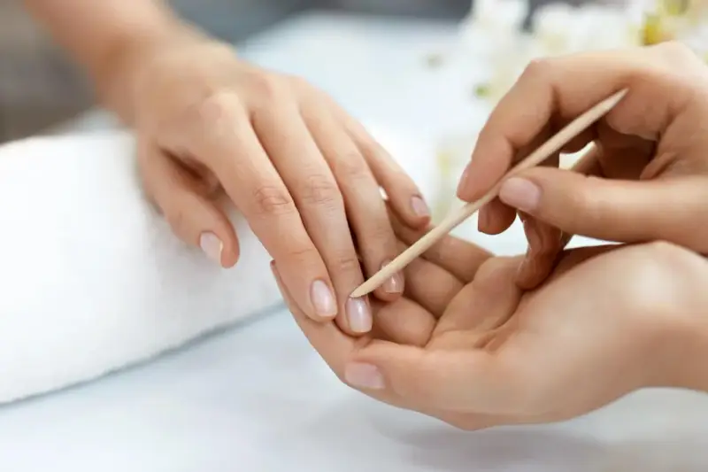 Delikatne dłonie poddawane zabiegowi manicure biologiczny. Skórki są starannie odsuwane patyczkiem, przygotowując paznokcie do dalszej pielęgnacji.